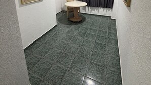 Une petite pièce étroite, avec un sol carrelé, une table ronde, une chaise et une fenêtre avec des rideaux.