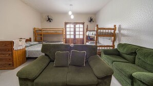 A room with bunk beds, a green sofa, a wooden dresser, and two wall fans. - Casa Para 6 Pessoas com Churrasqueira em Peru be (Peruíbe)