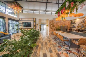 A modern kitchen with a brick wall, a dining area with wicker chairs, and a large potted plant in the center. - La Fortuna Garden Luxury Smart House private swimming pool. (La Fortuna)