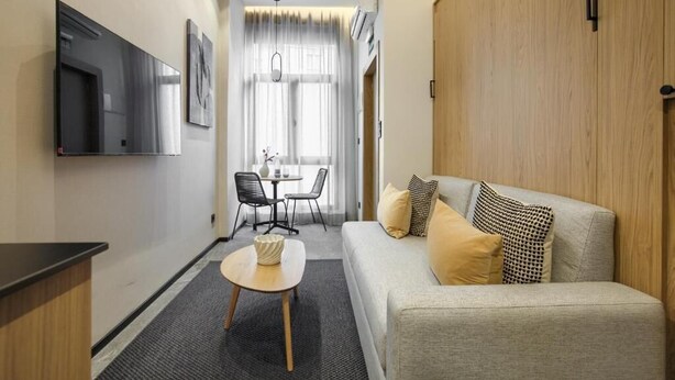 Una camera d'albergo moderna con divano, tavolino, televisione e zona pranzo con sedie e tavolo.
