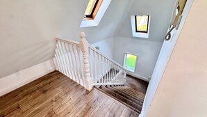Een trap met houten vloer en witte balustrades, leidend naar een verdieping met dakramen.