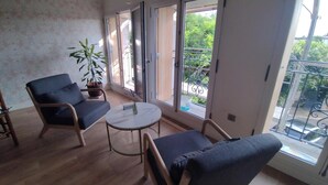 A room with a wooden floor, a blue sofa, a small round table, and a potted plant. - Le Petit Molière Gîte for 2 people (Servian)