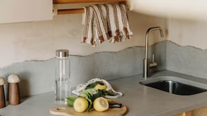 A kitchen counter with a cutting board, lemons, a knife, a water bottle, and a cloth hanging above a sink. - Mason and Fifth - Belsize Park (London)