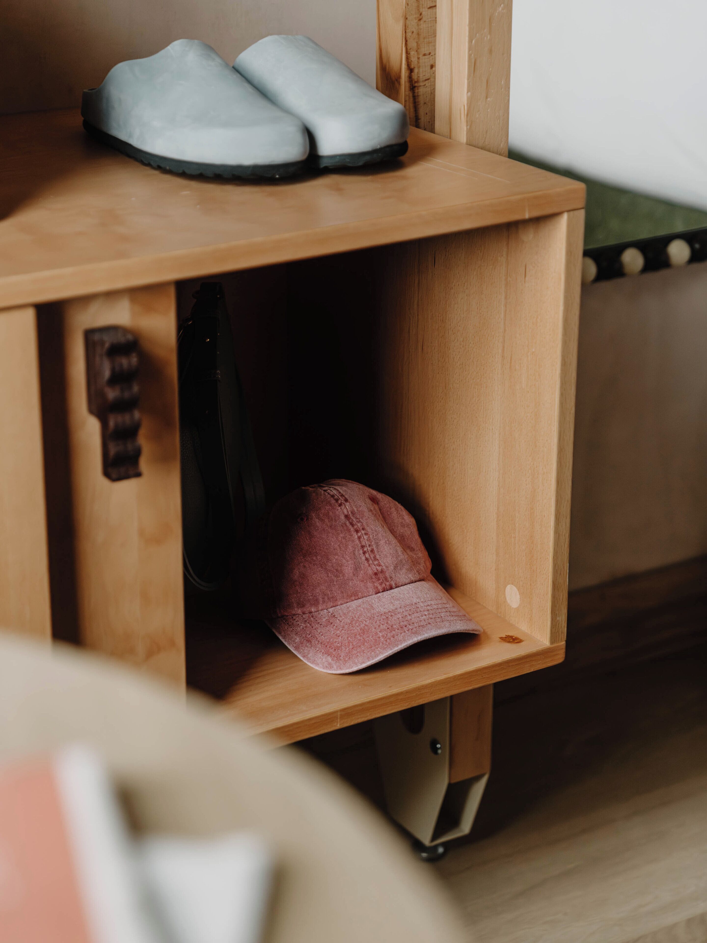 A wooden shoe rack with a pair of shoes and a cap.