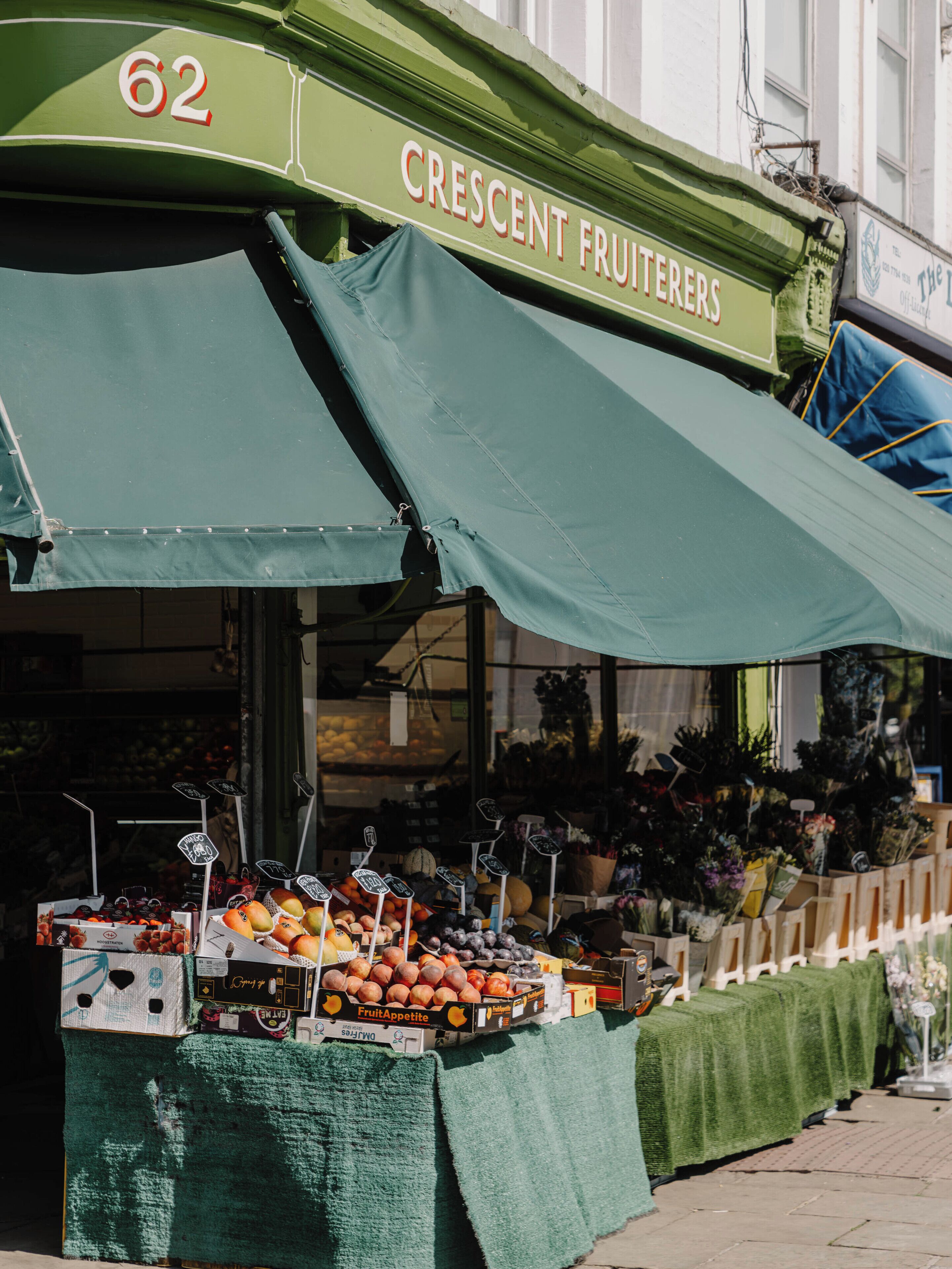 Een kraam met fruit, voorzien van een groen luifel waarop 'Crescent Fruiters' staat en het nummer '62'.