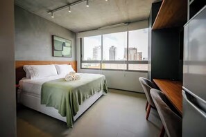 A hotel room with a bed, a desk, a chair, a window with a city view, and a flat-screen TV. - DOMINGO DE MORAES 1008 (São Paulo)
