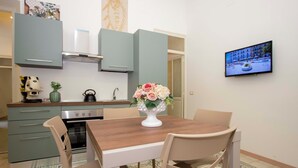 Eine moderne Küche mit Esstisch, Stühlen, einem an der Wand befestigten Fernseher und einer dekorativen Vase auf dem Tisch.