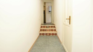 Ein Korridor mit Fliesenboden, einer Tür mit Messinggriff und einer weißen Wand.
