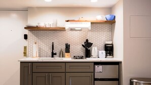 Ett kompakt kök med ett hexagonalt kakel som stänkskydd, en inbyggd spis, en kaffebryggare och ett kylskåp i rostfritt stål.