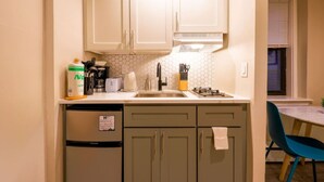 A compact kitchen with white cabinets, a dishwasher, a coffee maker, and a sink. - Stylish Studio in South End (Boston)