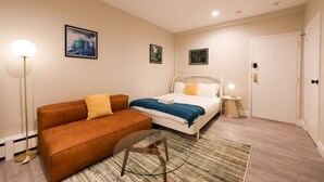 A bedroom with a bed, a sofa, a chair, and a floor lamp. - Stylish Studio in South End (Boston)