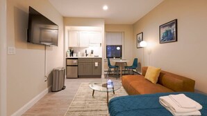 A compact hotel room with a kitchenette, a sofa, a small round table, and a TV mounted on the wall. - Stylish Studio in South End (Boston)