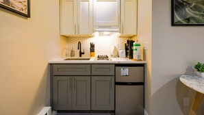 A compact kitchen with white cabinets, a black faucet, and a small refrigerator. - Studio Nestled in Back Bay! (Boston)