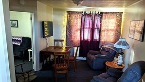 A living room with a sofa, a dining table with chairs, a television, and a lamp. - Peaceful 2-bedroom apartment with AC in charming Canaan (Canaan)