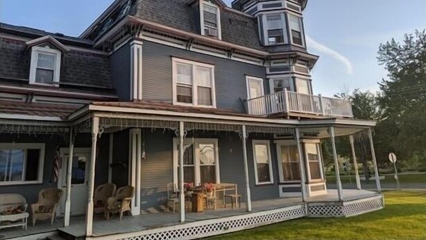 A large, two-story house with a prominent tower and a covered porch with outdoor furniture. - Peaceful 2-bedroom apartment with AC in charming Canaan (Canaan)