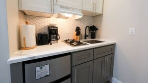 A compact kitchen with a gas stove, coffee maker, and a sink. There are cabinets above and below the counter, and a sign on the lower cabinet. - Vibrant Studio | Prudential Area (Boston)