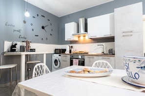 A modern kitchen with a clock, washing machine, and dining area with a plate of food. - Apartment 'Oasi Giardinello' with Wi-Fi and Air Conditioning (Agrigento)