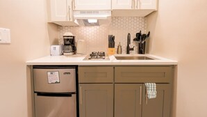 Eine kleine Küchenzeile mit integriertem Kühlschrank, einer Kaffeemaschine, einem Toaster und einer Spüle mit Messerblock.