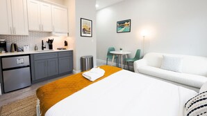 Ein modernes Hotelzimmer mit Bett, einer kleinen Küchenzeile, einer Essecke mit Tisch und Stühlen sowie einem Sofa.