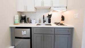 Eine kleine Küche mit weißen Schränken, einem Edelstahl-Kühlschrank, einer Kaffeemaschine, einem Toaster und einem Gasherd.