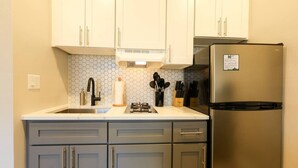 A kitchen with light-colored cabinets, a stainless steel refrigerator, a sink with a faucet, and a hexagonal tile backsplash. - Spacious Studio | Prudential Area (Boston)