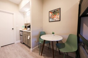 A compact kitchen with a dining area, featuring a round table and two chairs, a small potted plant, and a framed picture on the wall. - Loft Bed Studio | Prudential Area (Boston)