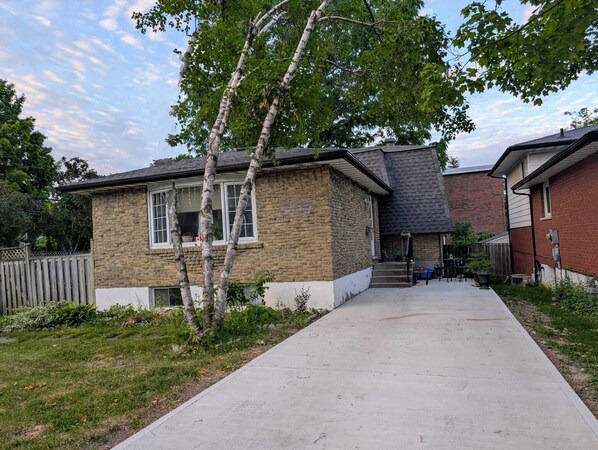 A two-story brick house with a front porch and a concrete walkway leading to the entrance. - Comfortable Private Room in Shared Bungalow | Near Hospital, Schools & Shopping (Peterborough)