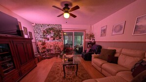 A living room with a sofa, a coffee table, a cabinet, and a ceiling fan. - Comfortable Private Room in Shared Bungalow | Near Hospital, Schools & Shopping (Peterborough)