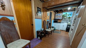 A cozy room with a wooden floor, a chair, a small table, and a kitchen area visible through an open door. - Comfortable Private Room in Shared Bungalow | Near Hospital, Schools & Shopping (Peterborough)