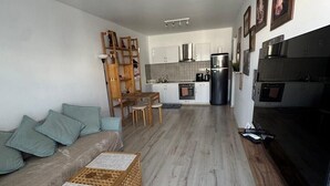 Een moderne keuken met roestvrijstalen apparatuur, een eetgedeelte met een houten tafel en stoelen, en een grijze bank met turquoise kussens.