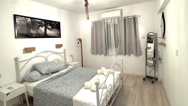 Een slaapkamer met een bed, nachtkastje, wandairconditioning en een raam met gordijnen.