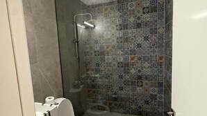 Een badkamer met een douche, toilet en een betegelde muur met een patroon.