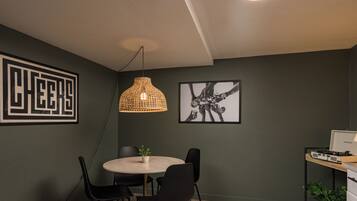 Une pièce moderne avec une table ronde, des chaises noires, un luminaire suspendu en fibres tressées et une œuvre d’art abstraite encadrée.