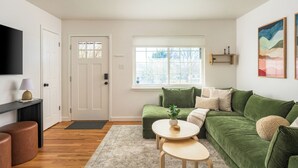 A modern living room with a green sofa, a small round table, and a TV mounted on the wall. - Spacious home w/HotTub, Game Room, Backyard Oasis - near Denver/Boulder+Pets OK! (Westminster)
