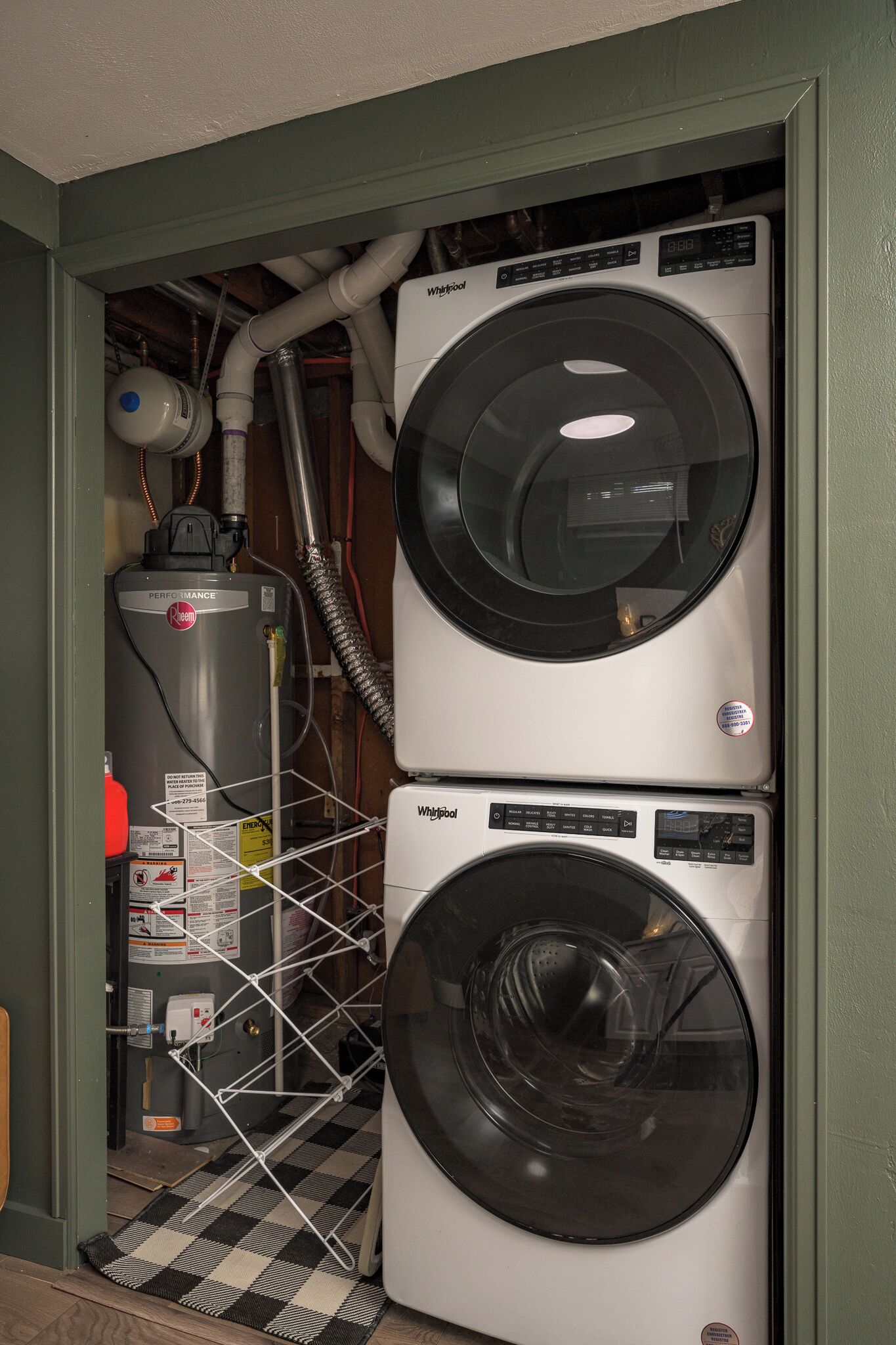 Pequeña sala de lavandería con dos lavadoras Whirlpool apiladas y un calentador de agua.
