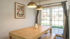 A dining area with a wooden table, two pendant lights, a vase, and a framed floral artwork. - Spacious home w/HotTub, Game Room, Backyard Oasis - near Denver/Boulder+Pets OK! (Westminster)