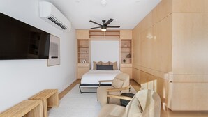 Ein modernes Schlafzimmer mit Bett, Sessel, Schreibtisch, Einbauschränken und Deckenventilator.