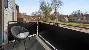 Ein Balkon mit einem schwarzen Stuhl und Blick auf eine Wohngegend, der Himmel ist wolkenlos.