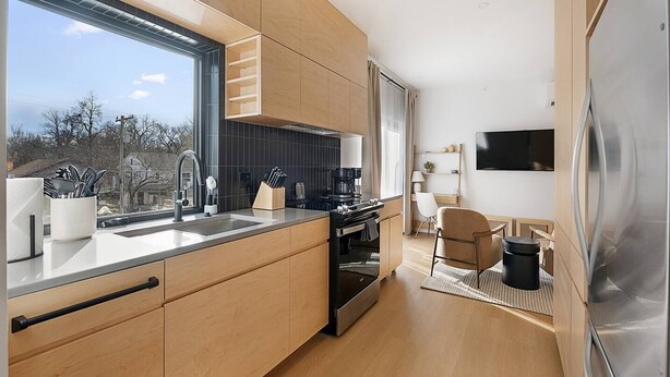 Eine moderne Küche mit großem Fenster, integrierten Geräten und einem Essbereich mit Fernseher.