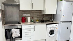 Una cucina moderna con mobili bianchi, una cappa in acciaio inossidabile, forno integrato, lavatrice e frigorifero.