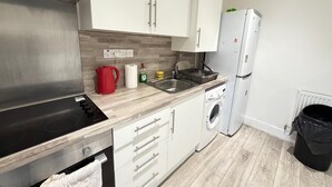 Una cucina moderna con mobili bianchi, una cappa aspirante in acciaio inossidabile, lavastoviglie integrata, una lavatrice e un frigorifero.