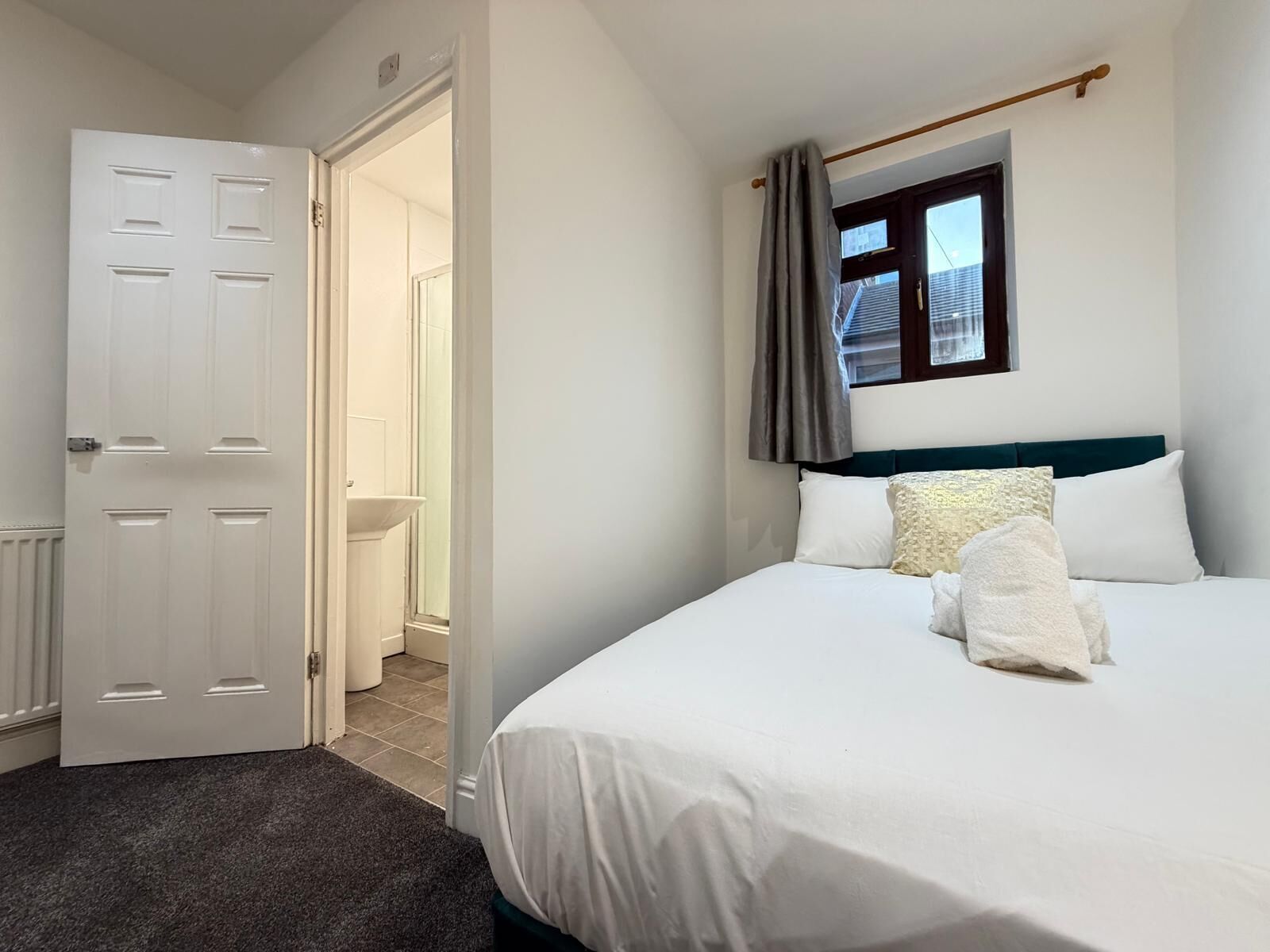 A hotel room with a bed, a window with curtains, a door, and a view of a bathroom.