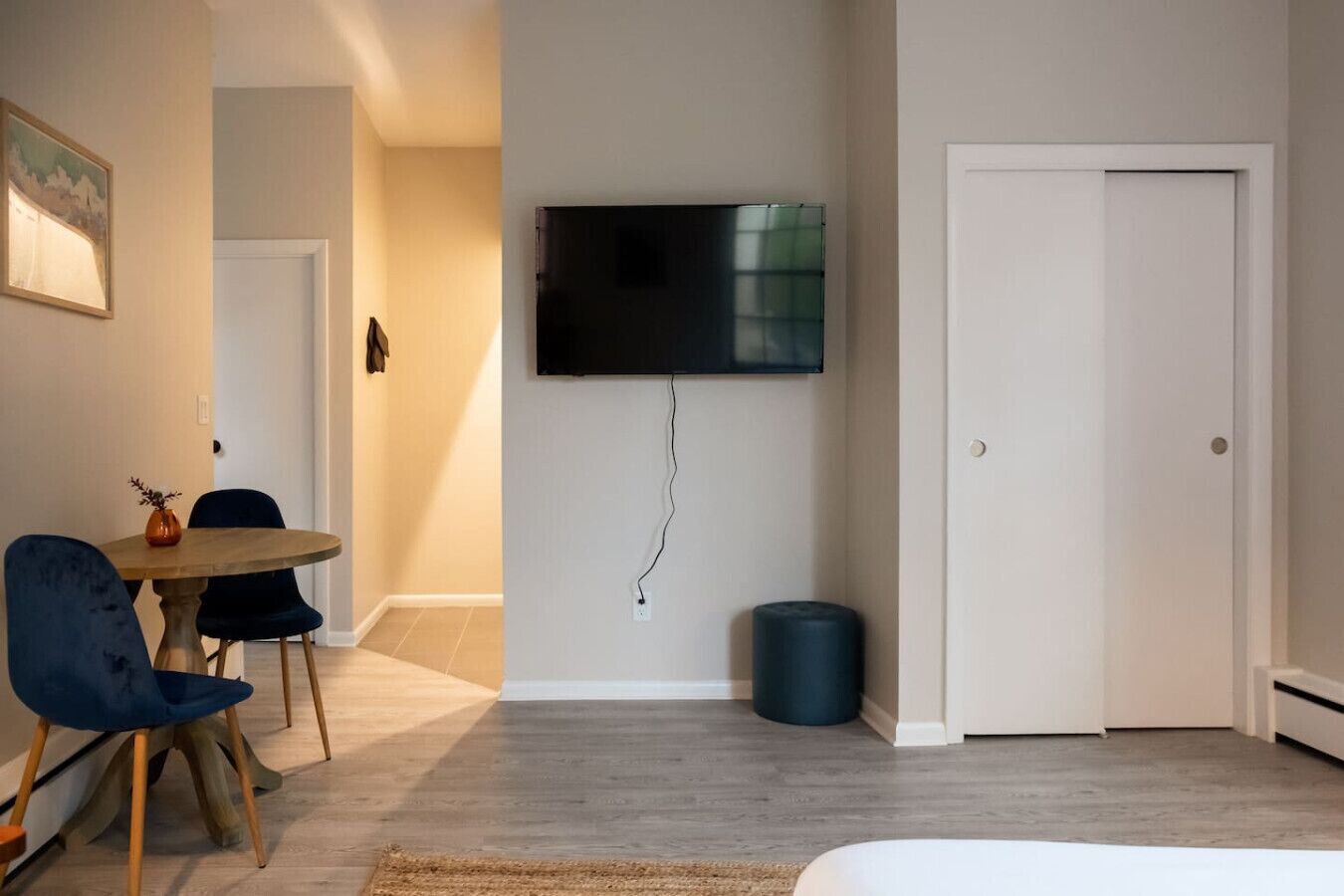A hotel room with a bed, a TV mounted on the wall, a dining area with a table and chairs, and a door.