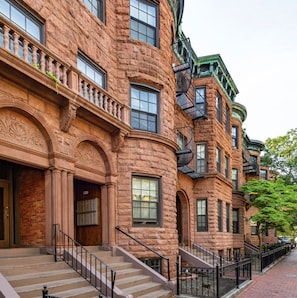 A row of brick townhouses with ornate architectural details, large windows, and a central staircase. - Modern Studio | South End (Boston)