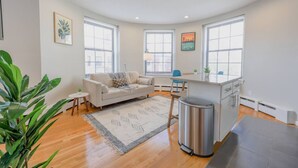 A modern living room with a sofa, a small table, and a kitchen area with a sink and countertop. - Light-filled Studio | Back Bay (Boston)