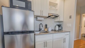 A modern kitchen with stainless steel appliances, white cabinetry, and a hexagonal tile backsplash. - Light-filled Studio | Back Bay (Boston)