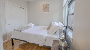 A bedroom with a bed, white towels, a bedside lamp, and a window. - Light-filled Studio | Back Bay (Boston)
