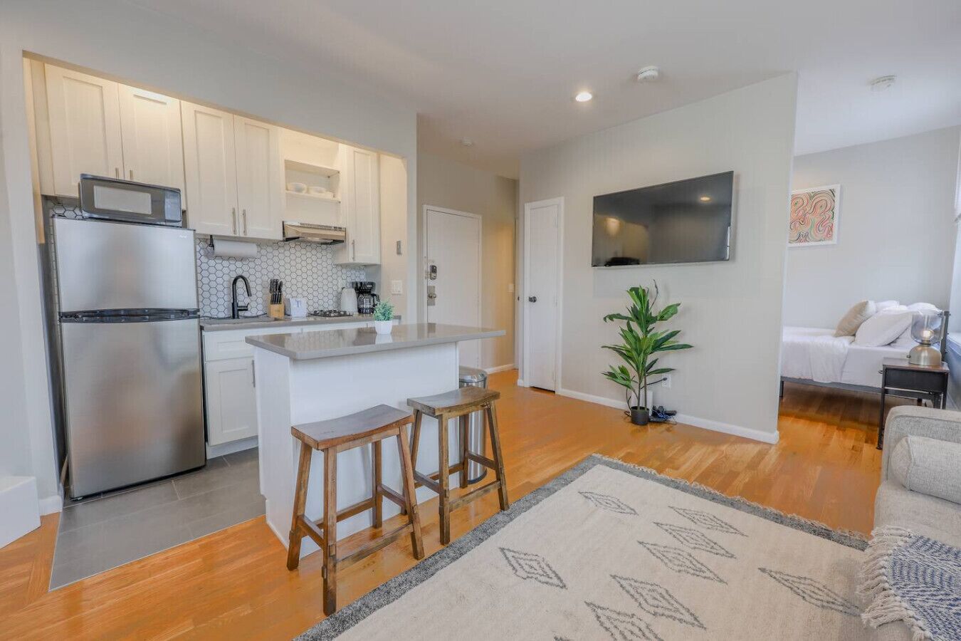 A modern kitchen with stainless steel appliances, a central island with stools, and a dining area with a sofa and a TV.