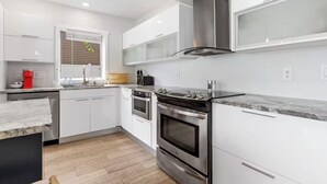 Une cuisine moderne avec des meubles blancs, des appareils en acier inoxydable et un parquet en bois disposé en chevrons.