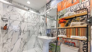Une salle de bain avec une douche en marbre, un lavabo sur colonne et des toilettes. On y trouve des étagères avec des serviettes et des articles de toilette.